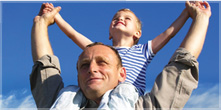 A boy sitting on the shoulders of an adult male guardian gesturing triumphantly